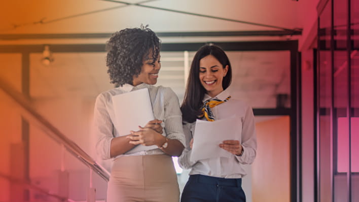 Two women carry files walking in an office